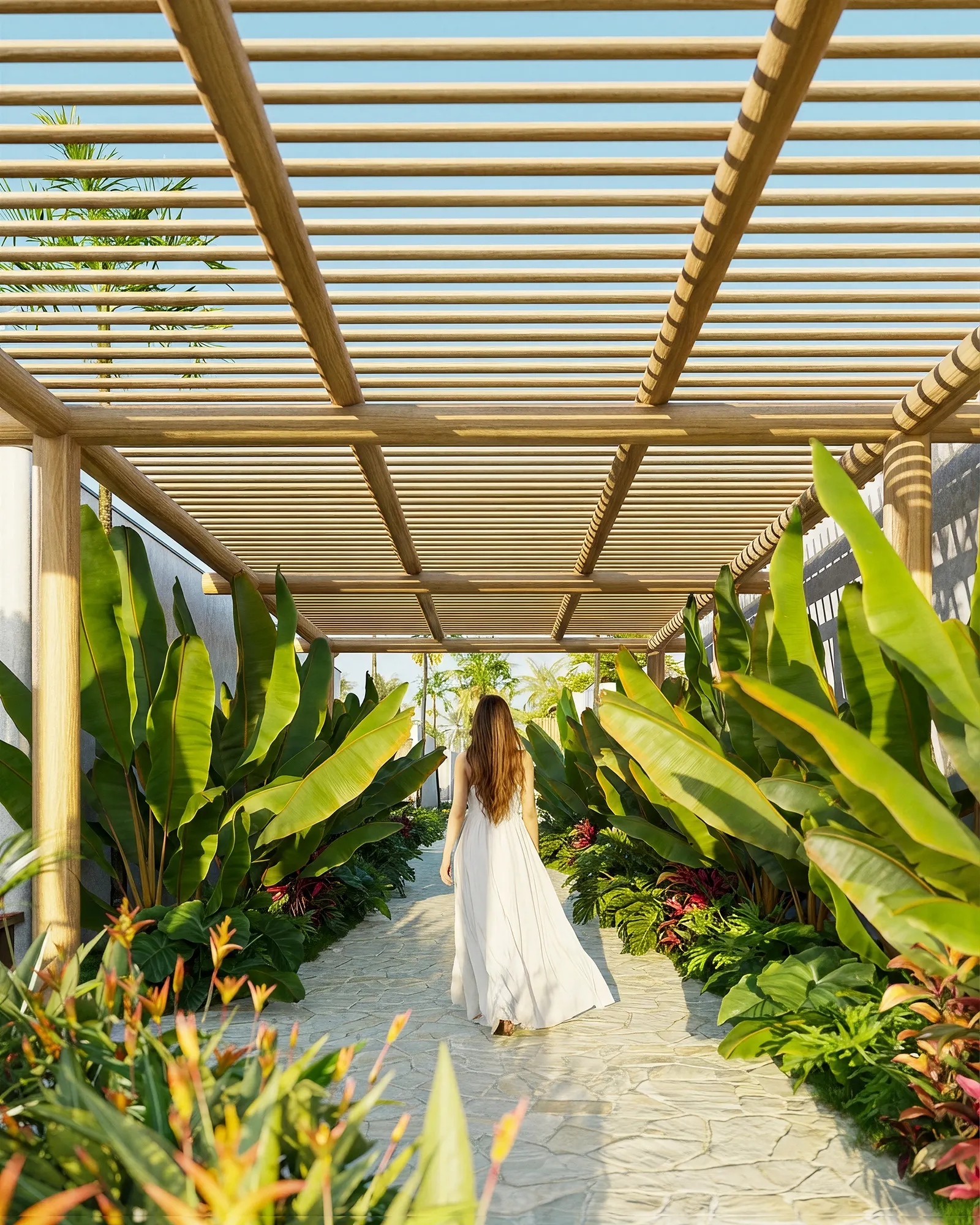 Mulher caminhando por um caminho de pedra sob uma pérgola de madeira, entre plantas tropicais.